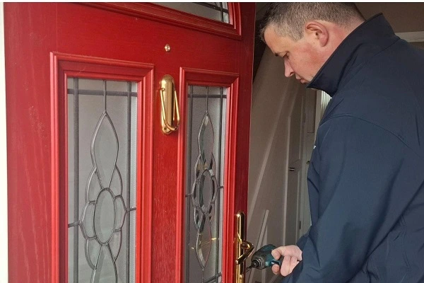 Locksmith removing a multipoint locking mechanism from a red composite door for repair or replacement.